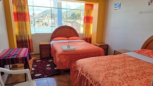Une chambre d’hôtel avec deux lits, une petite table, une chaise et une fenêtre avec des rideaux.