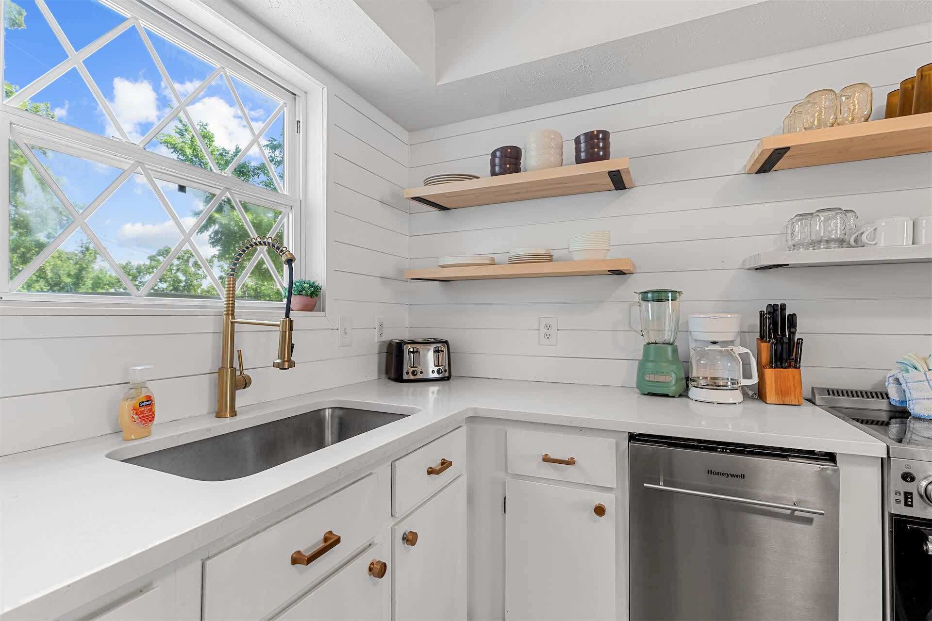A kitchen with white cabinetry, a stainless steel sink, a toaster, a blender, and a dishwasher.