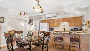 A modern kitchen with wooden cabinets, a central island with bar stools, and a dining area with a round table and chairs. - All Fore the Best | Onsite amenities (Branson)