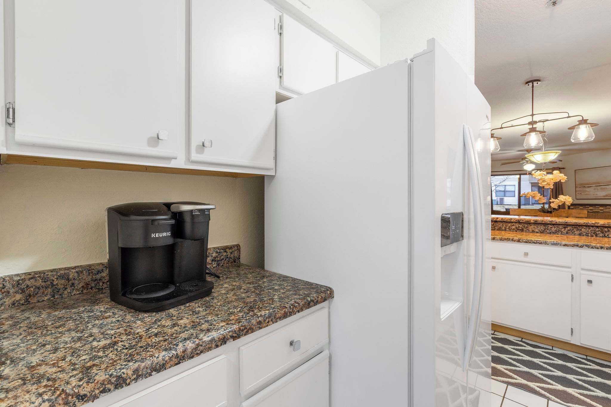 A kitchen with white cabinets, a granite countertop, a coffee maker, and a refrigerator.