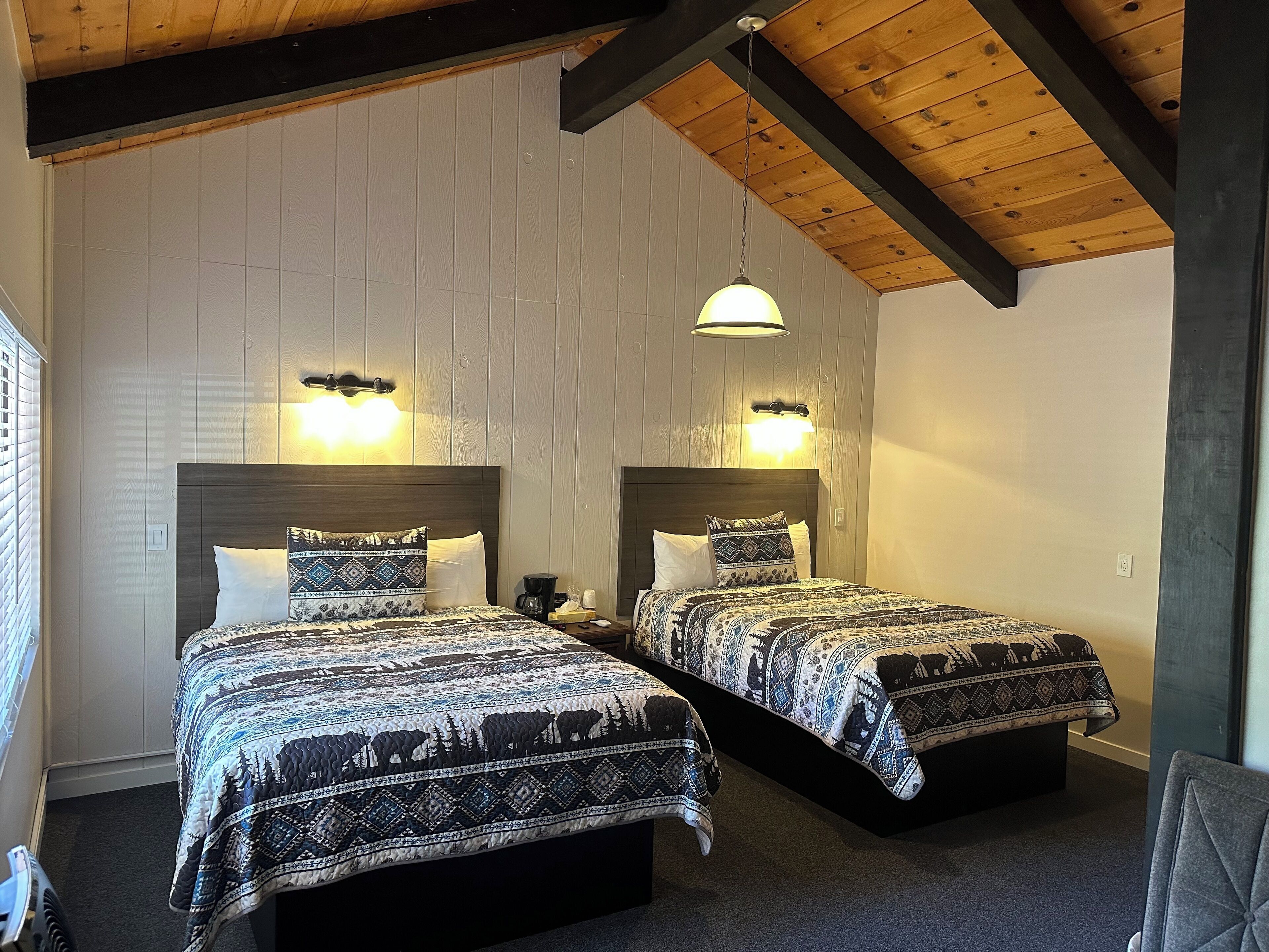A room with two beds, each with patterned bedding, wooden headboards, and wall-mounted lights.
