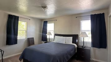 Une chambre à coucher comprenant un lit, deux tables de chevet, une chaise et deux fenêtres avec des rideaux.