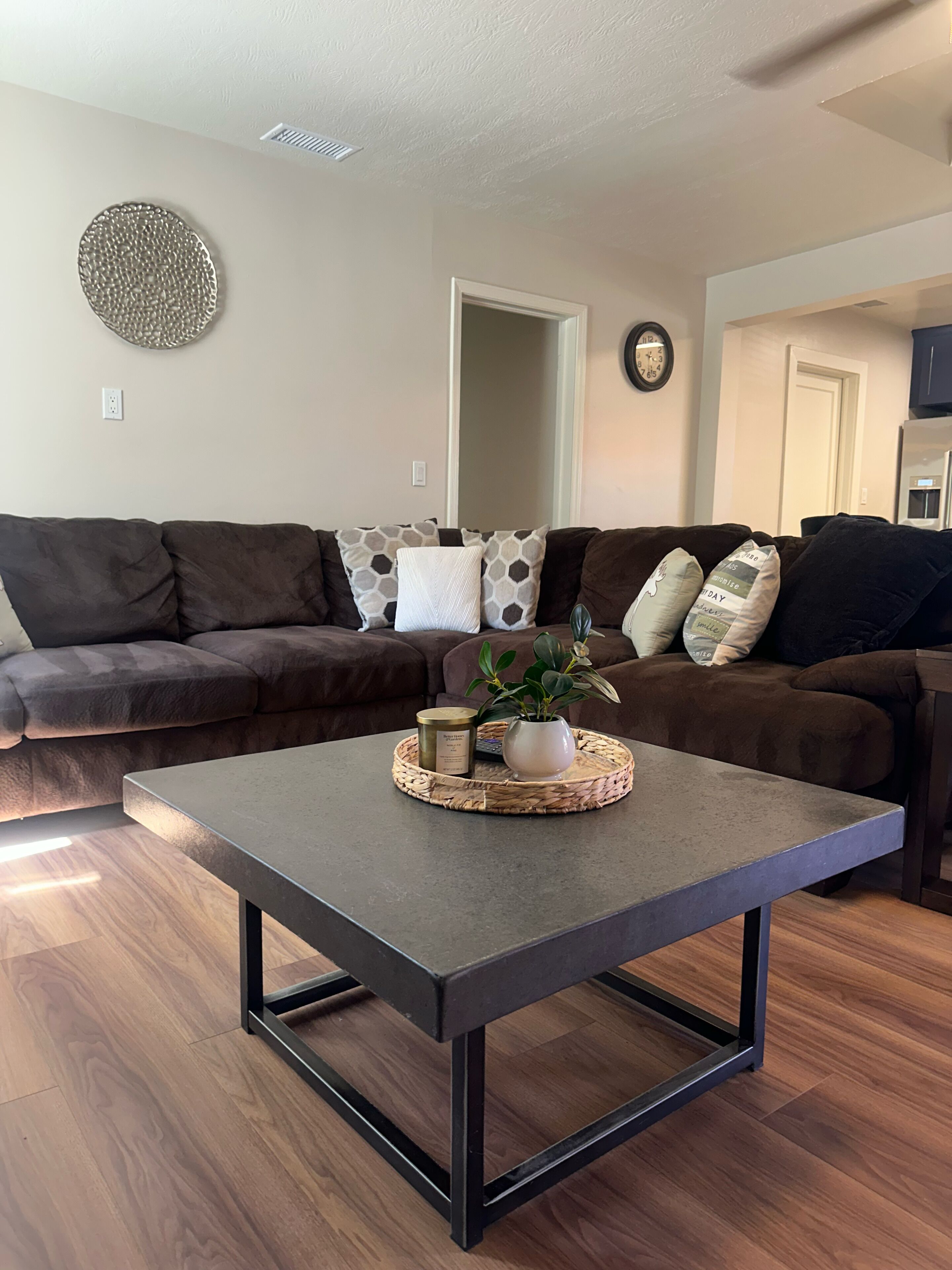 A living room with a dark brown sofa, a woven coffee table, and a potted plant.