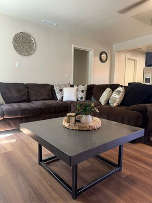 A living room with a dark brown sofa, a woven coffee table, and a potted plant. - Lee Vining Motel (Lee Vining)