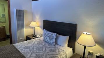 Ein Hotelzimmer mit einem Bett, zwei Nachttischlampen, einem Nachttisch, einem hölzernen Kopfteil und einer Wand-Klimaanlage.