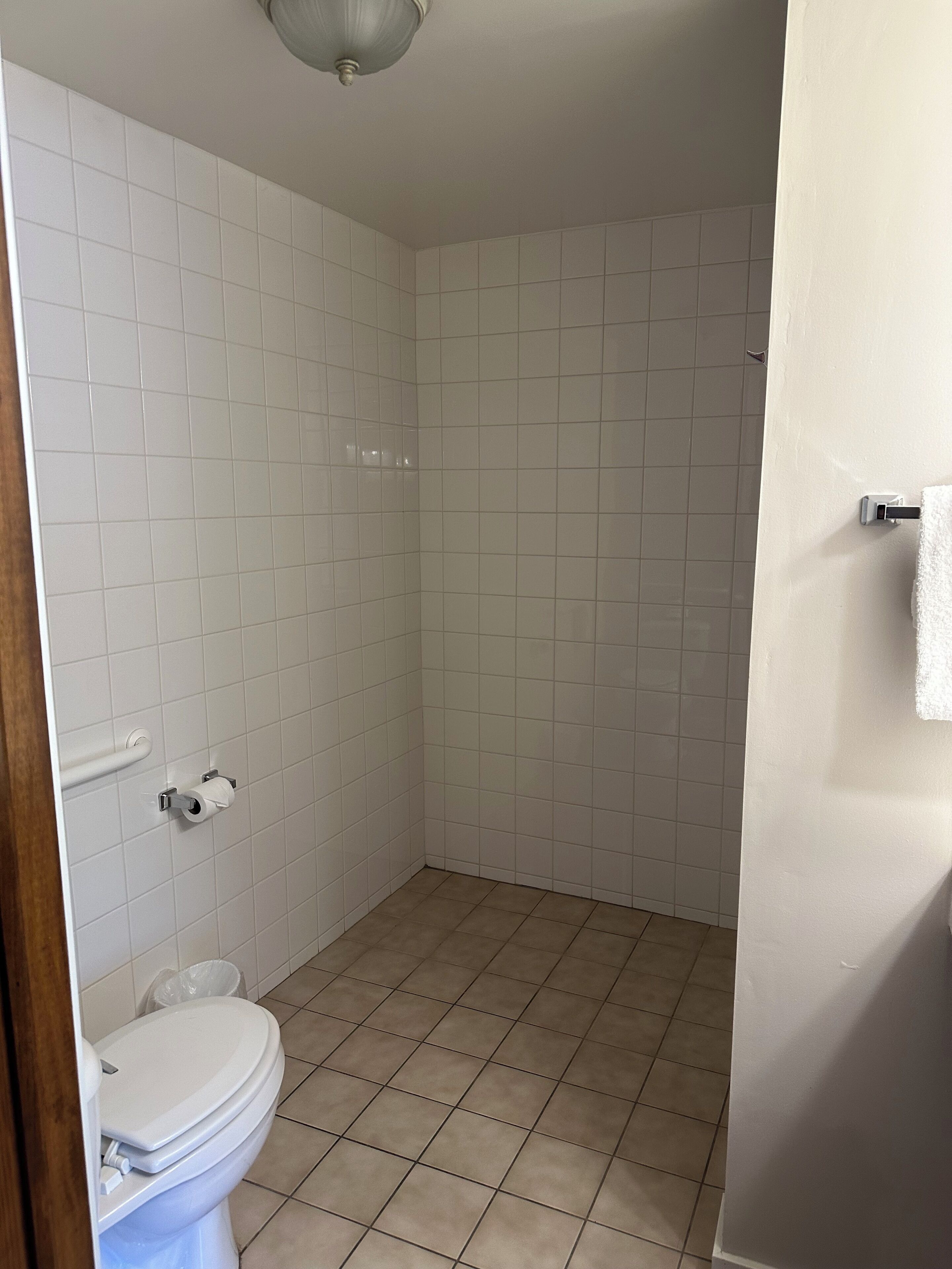 Une salle de bain avec des murs recouverts de carreaux blancs, des toilettes, un espace douche et un luminaire au plafond.