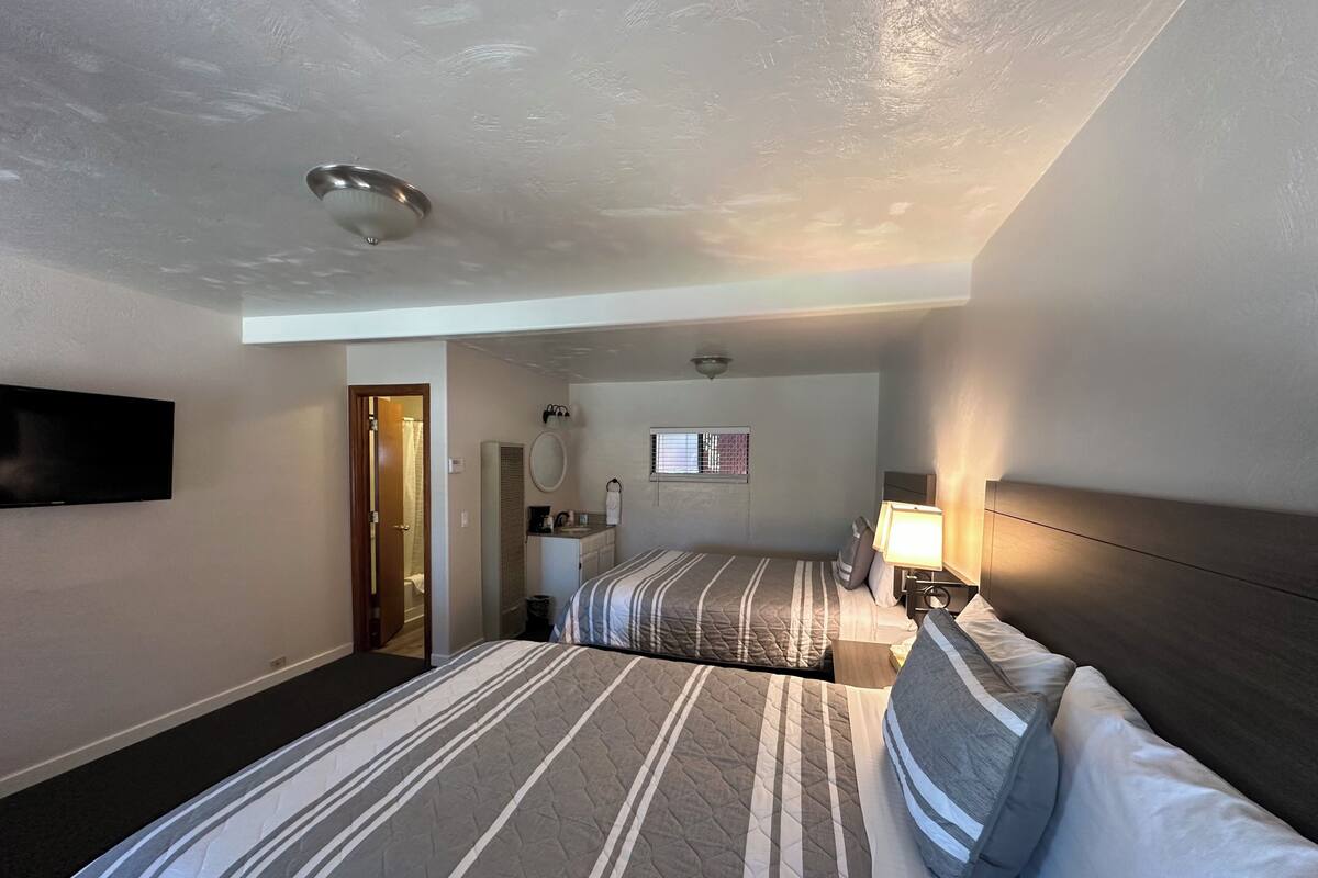 Habitación de hotel con dos camas, televisión, baño y un escritorio pequeño con lámpara.