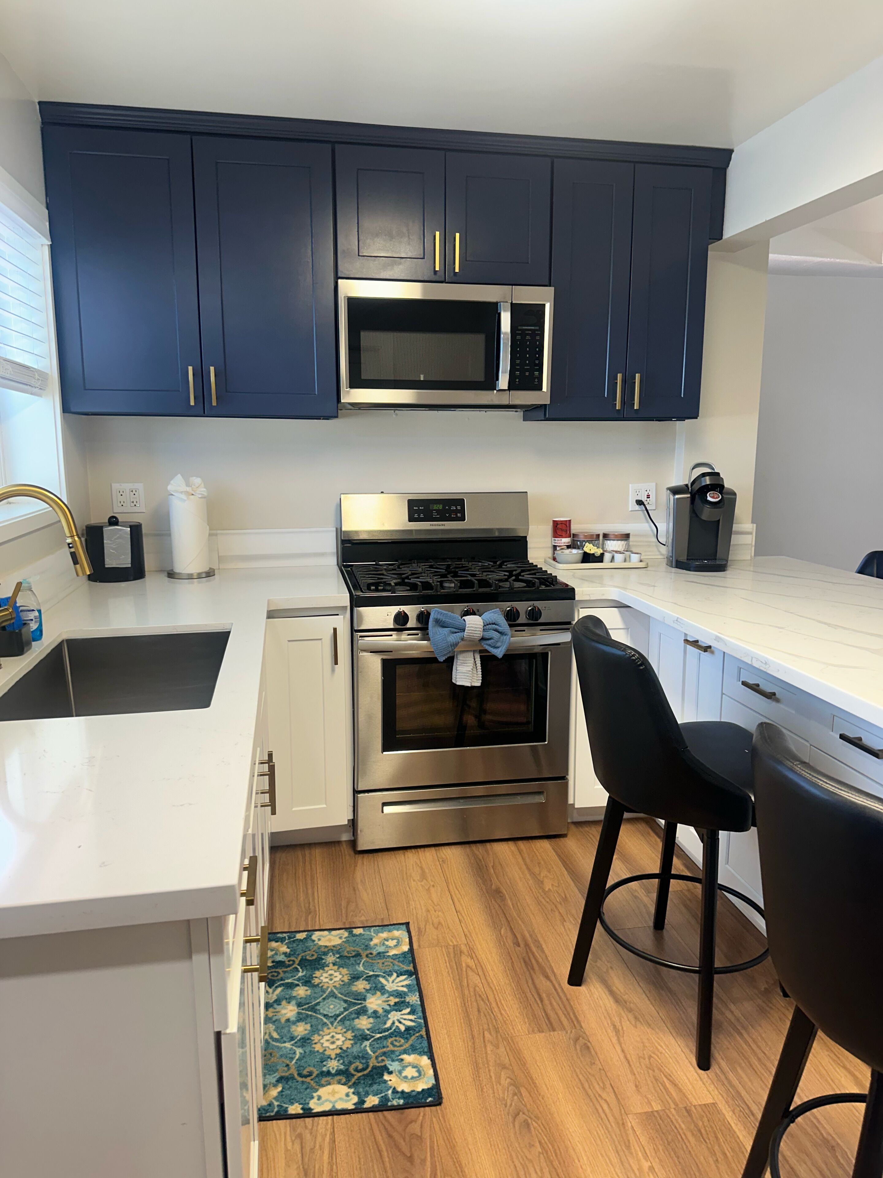 Uma cozinha moderna com armários azul escuro, eletrodomésticos de aço inoxidável, bancada branca e piso de madeira.