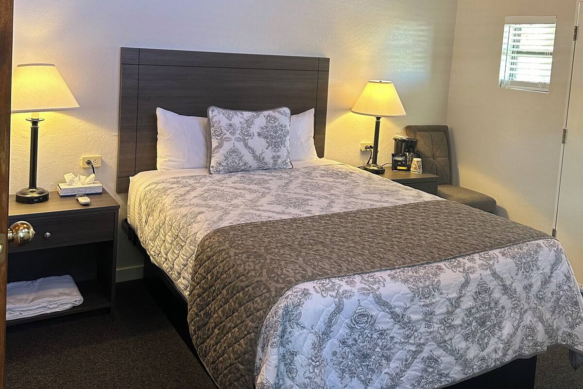 Habitación de hotel con techo de madera, una cama grande con colcha estampada, dos mesitas de noche con lámparas y un ventanal pequeño.