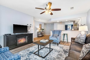 A living room with a fireplace, a ceiling fan, a TV, and a dining area in the background.
