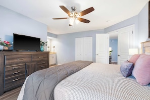 A bedroom with a bed, a dresser, a ceiling fan, and a television.