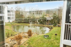 A view of a pond with a fountain, surrounded by grass and trees, with buildings in the background. - Brookside Haven – Gorgeous, Private Community! (Branson)