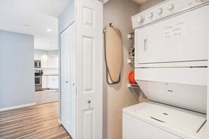 A laundry room with a white dryer, an ironing board, and a note on the wall instructing to clean the lint filter after using. - Brookside Haven – Gorgeous, Private Community! (Branson)