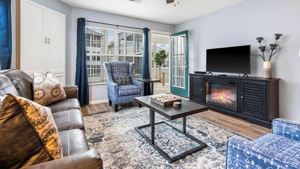 Una sala de estar con sofá, sillón, mesa de centro, chimenea, televisor y ventilador de techo.