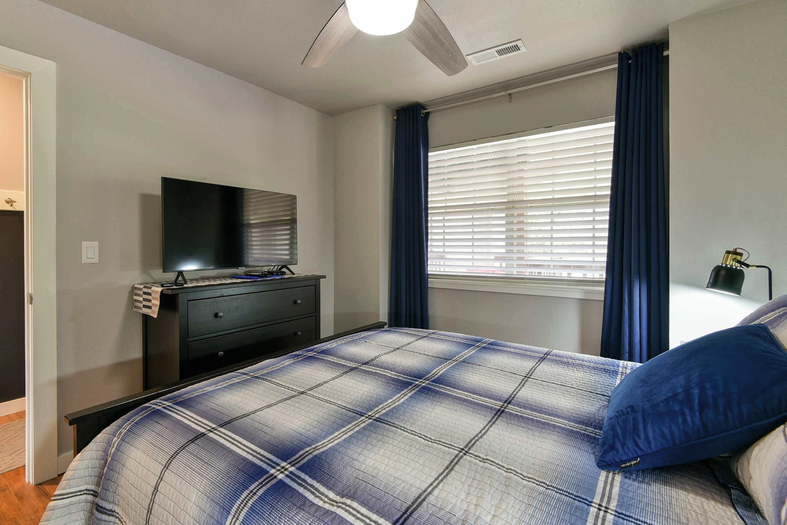 A bedroom with a bed, a dresser, a television, and a window with curtains.