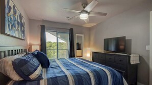 A bedroom with a bed, a television, a dresser, and a ceiling fan.