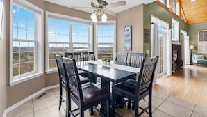A dining area with a large table and chairs, large windows, and a ceiling fan. - The Greenview Manor - Lake View - 9 Miles from Silver Dollar City (Kimberling City)