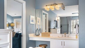 A bedroom with a white bed, a bedside table, a large mirror, and a window with curtains. - Eagle's Nest at The Club- Chic 2BR Golf View Condo (Branson)