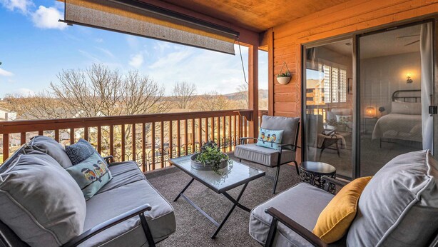 A balcony with a sofa, armchair, and table, a sliding glass door to a bedroom, and a view of the landscape. - Bright Stylish Condo w/ Balcony (Branson)