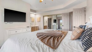 A bedroom with a bed, a ceiling fan, a flat-screen TV, a dresser, a mirror, and a door leading to another room. - Glorious Relaxation| Golf Course Views (Branson)