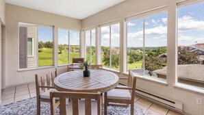 A sunlit room with a round wooden table and chairs, large windows offering a view of a green landscape, and a ceiling fan. - Glorious Relaxation| Golf Course Views (Branson)