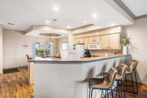 A modern kitchen with a central island, bar stools, and wooden cabinets.