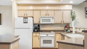Una cocina moderna con armarios de madera clara, microondas integrado, refrigerador y lavavajillas.