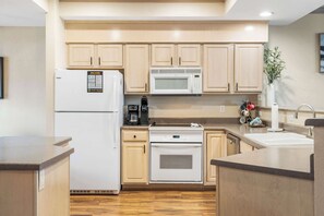 A modern kitchen with light wood cabinets, a built-in microwave, a refrigerator, and a dishwasher.