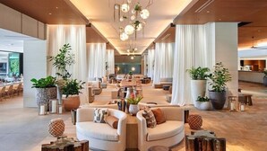 Een ruime lobby met een centraal zithoek, grote potplanten en een moderne kroonluchter.