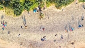 Luchtbeeld van een strand met helder turquoise water, een zandstrand en mensen verspreid over het strand.