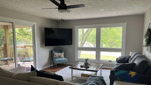 A living room with a ceiling fan, a flat-screen TV, a sofa, a chair, and a coffee table. - Charming 3-bedroom house across from Lake Freeman (Monticello)