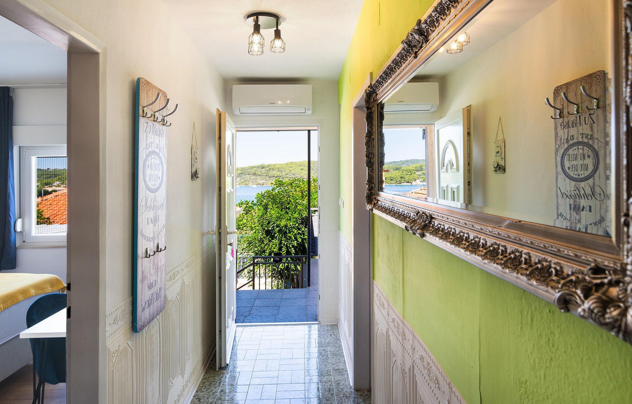 Un couloir donnant sur un balcon, un miroir avec un cadre décoratif et un lit recouvert d’une couvre-lit jaune.