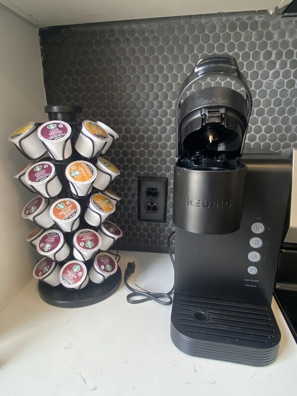 A Keurig coffee maker with a water reservoir and a mug holder with various coffee pods. - Optimum - Downtown Sanctuary! (Birmingham)
