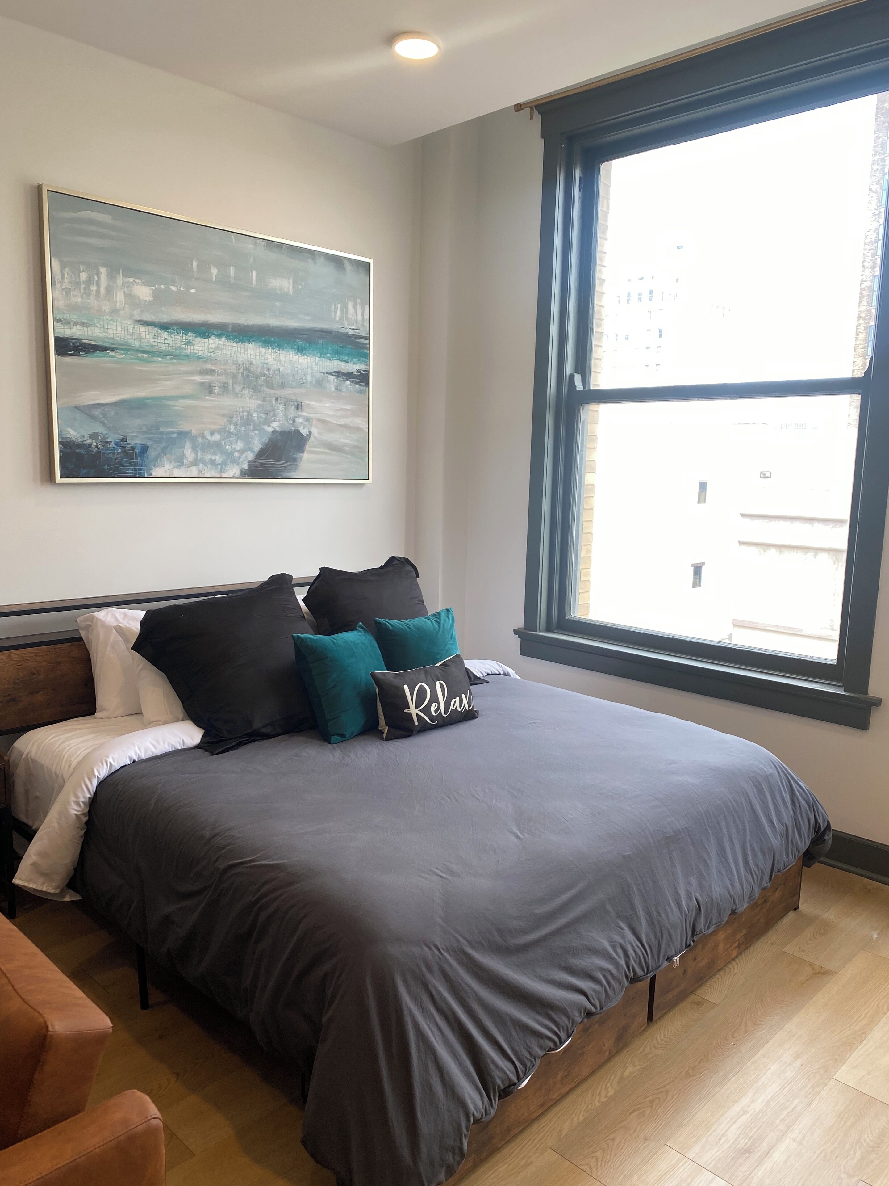 A bedroom with a large bed, a cityscape painting, and a window with a view of buildings.