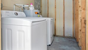 A laundry area with a Samsung self-cleaning washer and dryer, a water heater, and wooden framing. - Bungalow Near Downtown Orlando, Winter Park, Major Hospitals, and Disney! (Orlando)
