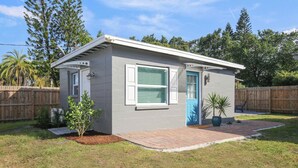 A small, single-story building with a grey exterior and a blue door, surrounded by a wooden fence and a grassy yard. - Bungalow Near Downtown Orlando, Winter Park, Major Hospitals, and Disney! (Orlando)