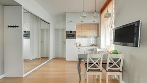 Een moderne keuken met witte kasten, een inbouwoven en een eethoek met een tafel en stoelen.