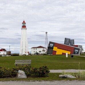 Un phare, un bâtiment moderne et un banc dans un espace verdoyant.