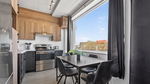 A modern kitchen with wooden cabinets, stainless steel appliances, and a dining area with a table and chairs. - Loft 301 | Rooftop | Downtown (Rimouski)