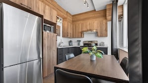 A modern kitchen with wooden cabinets, stainless steel appliances, and a dining table with chairs. - Loft 301 | Rooftop | Downtown (Rimouski)