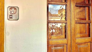 A wooden door with a glass panel, a number plaque, and a view of a building through the glass. - Hotel santone la ville (Villa de Leyva)