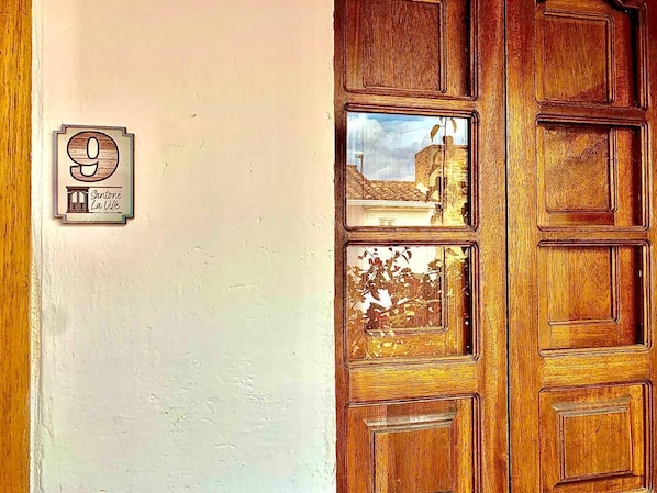 A wooden door with a glass panel, a number plaque, and a view of a building through the glass. - Hotel santone la ville (Villa de Leyva)