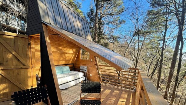 Una terraza de madera con una cama, dos sillas y barandilla de madera.