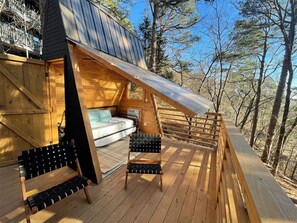 A wooden deck with a bed, two chairs, and a wooden railing.