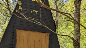 Una cabaña de madera triangular con una puerta grande de madera, una ventana pequeña y un buzón en la puerta.