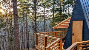 Una cabaña con terraza de madera y fachada azul oscuro, rodeada de un bosque.