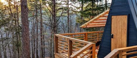 A cabin with a wooden deck and a dark blue exterior, surrounded by a forest.
