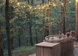 Uma banheira de hidromassagem em meio a uma floresta, iluminada por luzinhas.