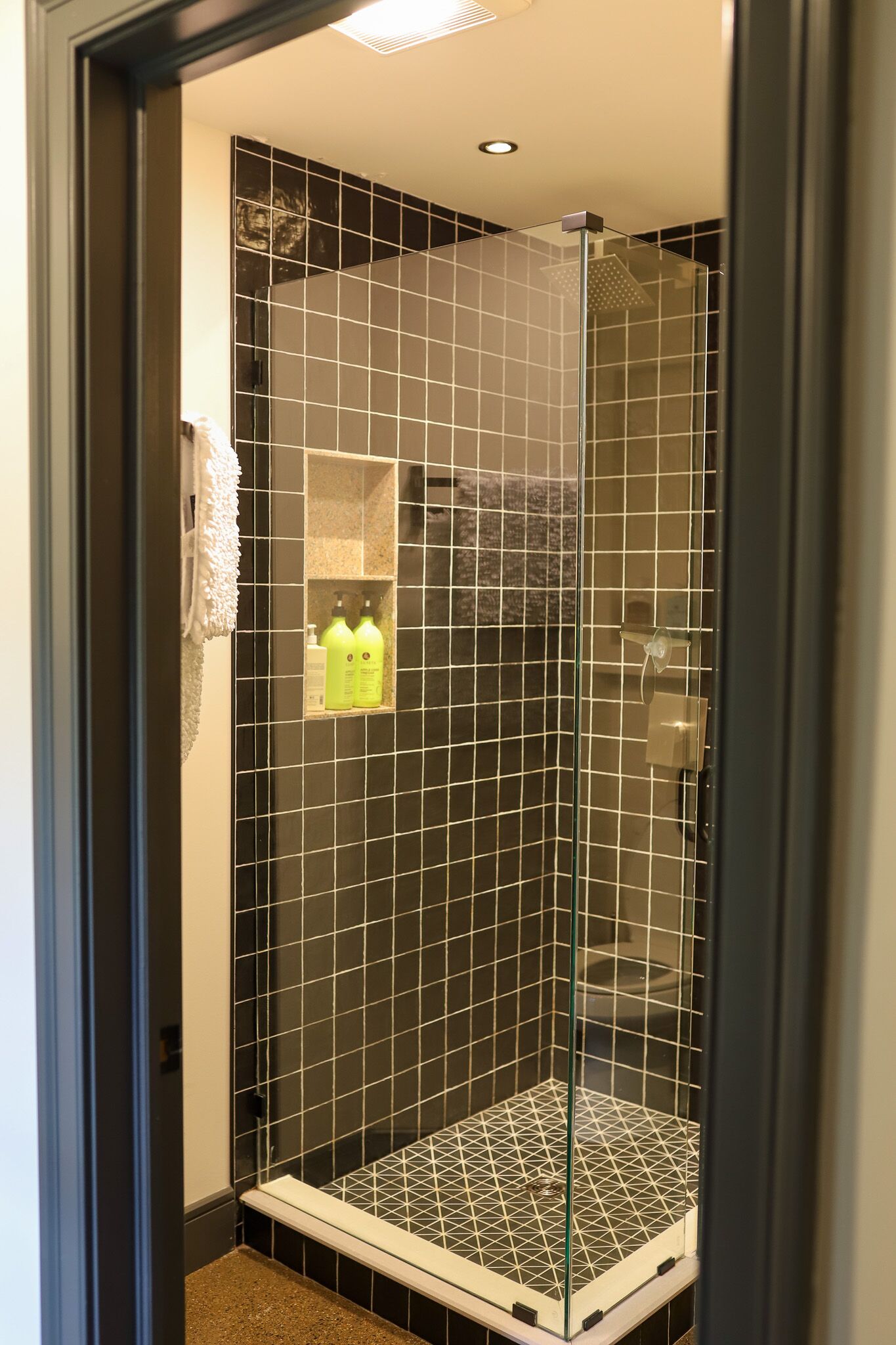 A glass-enclosed shower with a tiled floor and a small shelf with toiletries.