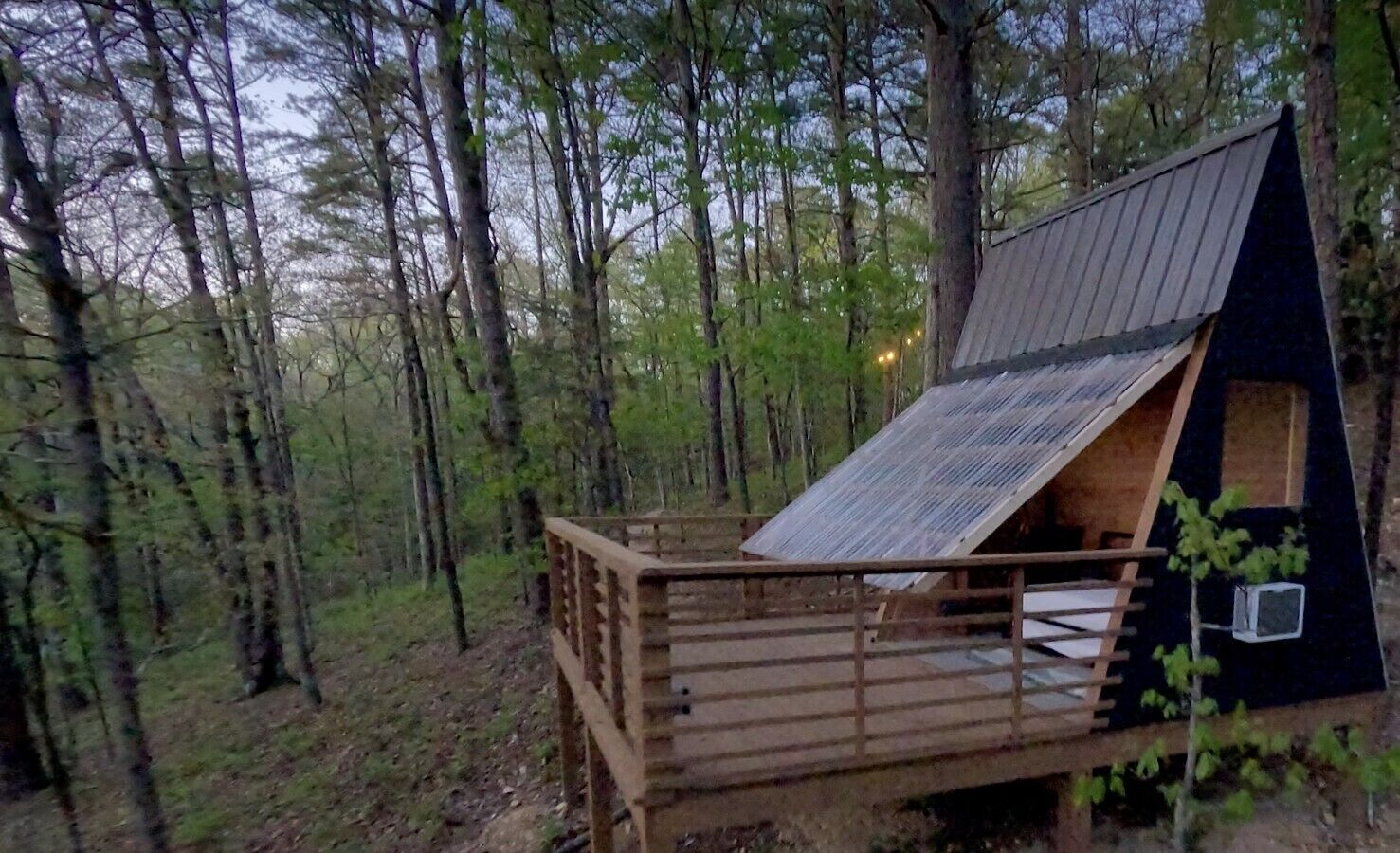 Une terrasse en bois avec une petite cabane, le tout entouré d’une forêt.